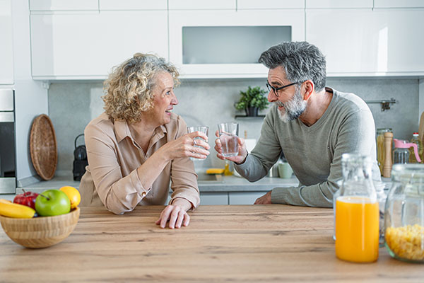 Cheerful mature couple drinking water and relaxing in the kitchen at home